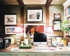 a desk with a computer, lamp and pictures on the wall