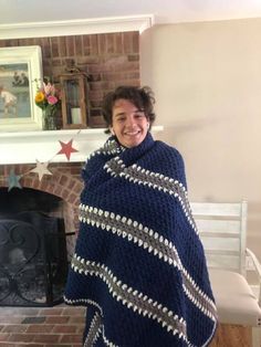 a smiling woman wrapped in a blue and white blanket by a fireplace with flowers on the mantle