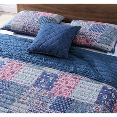 a bed with blue and pink quilted bedspread, pillows and pillow cases