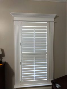 an empty room with white shutters in the corner and a lamp next to it