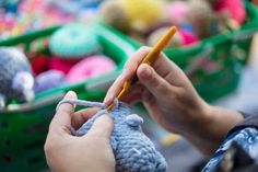 a person knitting something with a crochet hook in front of baskets full of balls of yarn