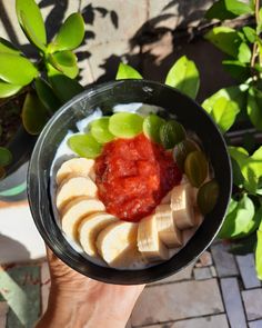 a person holding up a bowl of fruit with yogurt and sauce on top