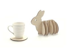 a cup and saucer are next to a wooden toy rabbit on a white background