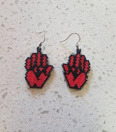 red and black beaded earrings with hand prints on them sitting on a white surface