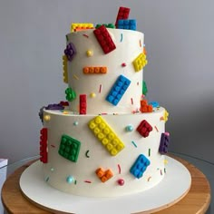 a white cake with legos on it sitting on top of a wooden table in front of a gray wall