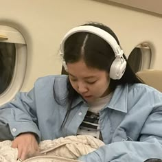 a woman wearing headphones is sitting on an airplane bed and looking at her phone