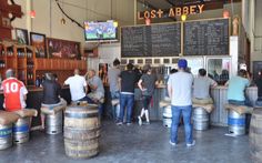 several people are standing at the bar in front of some beer kegs and televisions