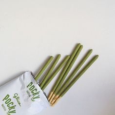 four green chopsticks in a bag on a white surface next to each other