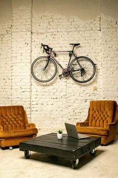 a living room with two chairs, a coffee table and a bike mounted to the wall