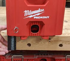 a person holding a red tool box on top of a piece of wood