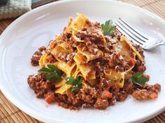 a white plate topped with pasta covered in ground beef and sauce next to a fork