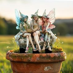 three fairy figurines sitting on top of a potted plant in the grass