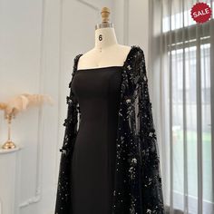 Elevate your evening look with the Dreamy Vow Luxury 3D Flowers Black Satin Arabic Evening Dress. The elegant mermaid silhouette is adorned with delicate 3D flowers and a stunning cape, adding a touch of sophistication. Made with high-quality satin, this dress is perfect for formal parties and special occasions. Experience elegance and luxury in our Dreamy Vow Arabic Evening Dress. Adorned with intricate 3D flowers, this black satin dress is perfect for formal parties. The accompanying cape adds Black Masquerade Dress With Sleeves, Black Mermaid Dress With Cape, Luxury Elegant Dress With Cape Sleeves, Luxury Black Dresses With Cape Sleeves, Luxury Black Dress With Cape Sleeves, Luxury Elegant Evening Dress With Cape Sleeves, Luxury Satin Evening Dress For Formal Occasions, Luxury Black Maxi Dress With Cape Sleeves, Luxury Black Gown For Party