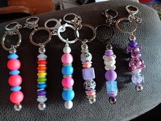 six key chains with different colored beads and charms hanging from them on a black leather surface