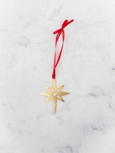 a gold star ornament hanging from a red ribbon on a white marble surface