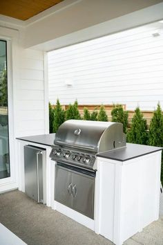 an outdoor kitchen with stainless steel appliances and grilling area in front of the house