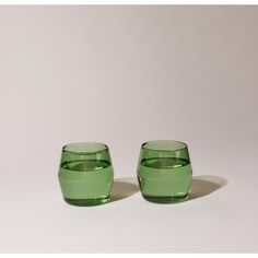 two green glasses sitting next to each other on a white surface with one empty glass in the middle