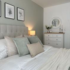 a bed with white sheets and pillows in a bedroom next to two framed pictures on the wall