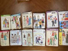 many vintage sewing patterns are laid out on a wooden table, including children's clothing