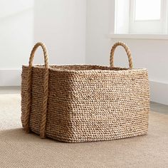 a large woven basket sitting on top of a floor next to a white wall and window