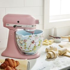 a pink mixer sitting on top of a counter next to doughnuts and croissants