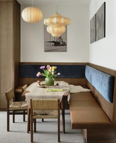 a table with some flowers on it in front of a bench and two lamps hanging from the ceiling