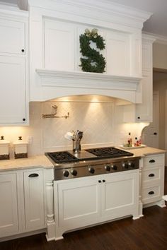 a kitchen with white cabinets and an oven in the center is lit by recessed lighting