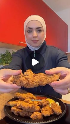 a woman is holding some fried food in her hands while wearing a headscarf