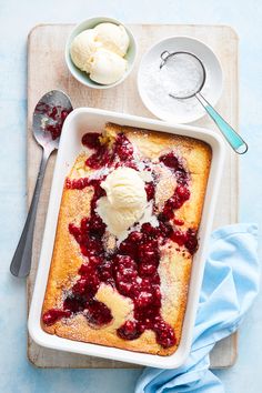 a dessert with ice cream and berries in a white dish on a cutting board next to spoons