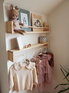 two wooden shelves with clothes hanging on them and a teddy bear sitting on top of the shelf