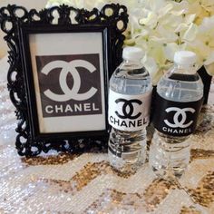 two water bottles are sitting on a table next to a chanel sign and flowers