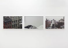 three pictures hanging on the wall in an art gallery with buildings and snow covered rooftops