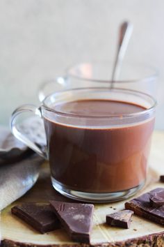 a glass cup filled with chocolate sitting on top of a wooden table next to pieces of bread