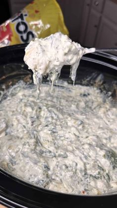 a crock pot filled with spinach and cheese being spooned into the slow cooker