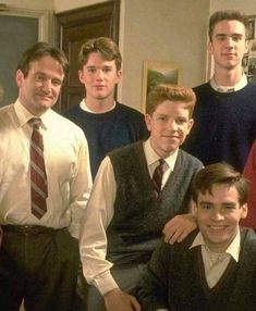 a group of young men standing next to each other in front of a door wearing sweaters and ties