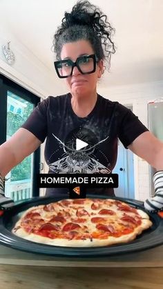 a woman with glasses is holding up a pizza