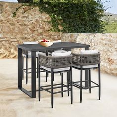 an outdoor table with four stools and a bowl of fruit on the counter top