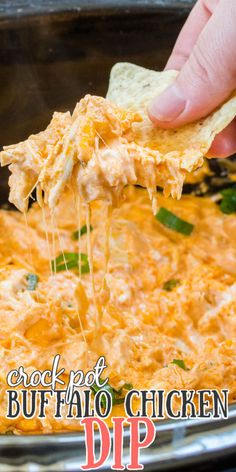 a hand holding a tortilla chip and dipping it into a casserole dish