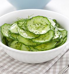 a white bowl filled with cucumbers on top of a checkered table cloth