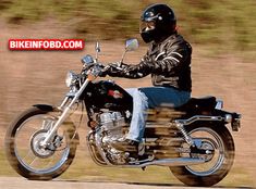 a man riding on the back of a black motorcycle down a road next to grass