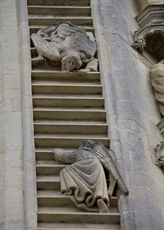 two statues on the side of a building next to a stair case that has been carved into it