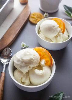 two white bowls filled with ice cream and orange slices on top of a black table