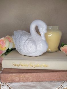 a white swan figurine sitting on top of a book next to a candle