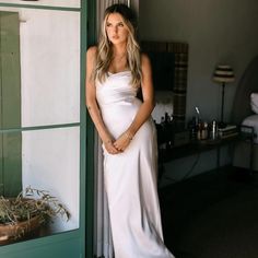 a woman in a white dress leaning against a wall with her hands on her hips