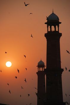 the sun is setting behind two towers with birds flying around