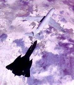 two fighter jets flying in the sky above some snow covered ground with clouds behind them