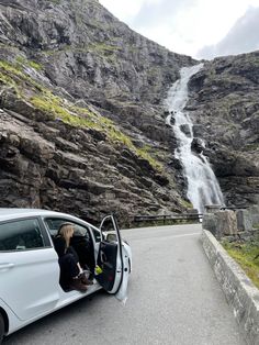 a white car parked next to a waterfall on the side of a road with its door open