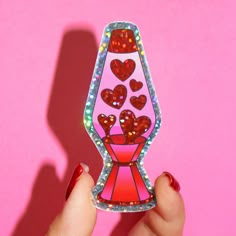 a hand holding up a pink sticker with hearts on it's top and bottom