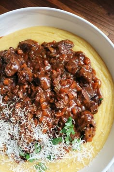 a white bowl filled with meat and cheese on top of a wooden table next to a fork