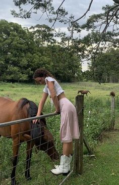 a woman standing next to a fence petting a horse